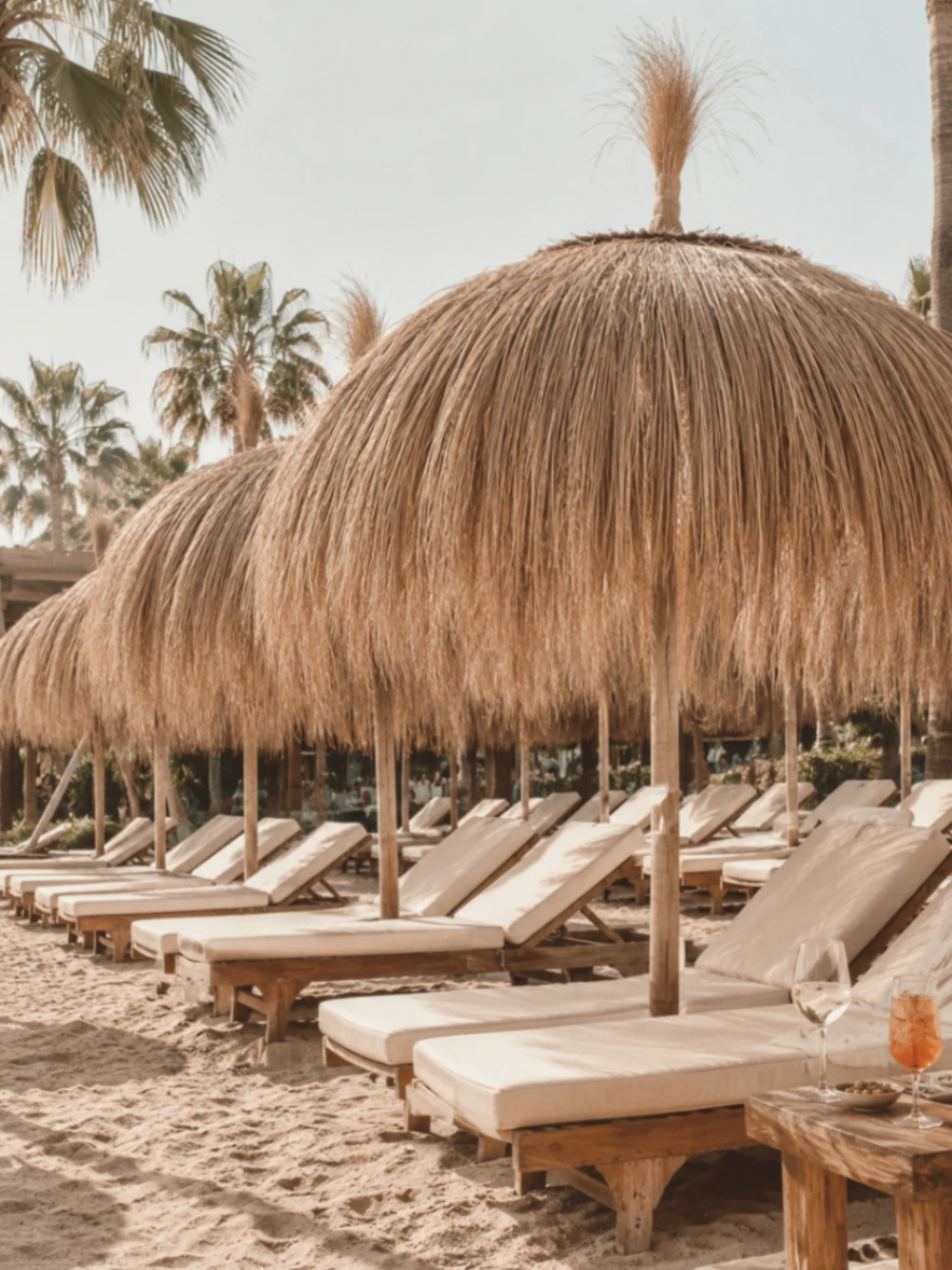 Front-row sunbeds at Trocadero Arena Marbella beneath oversized raffia parasols on the sand