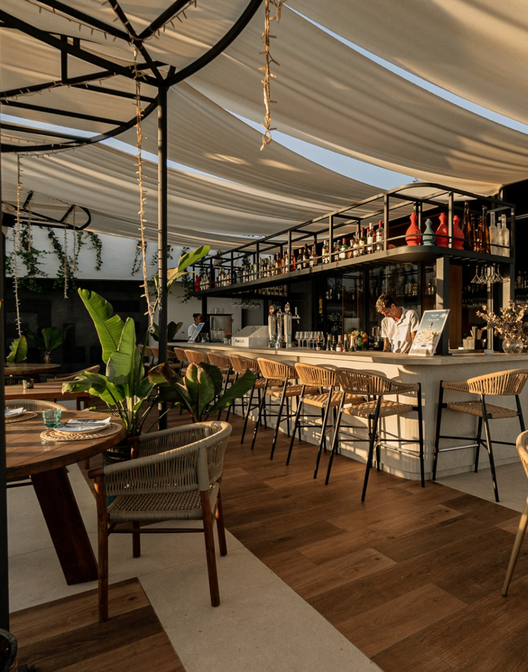 Open-air bar and lounge at Alabardero Beach Club with woven stools and soft canopy light