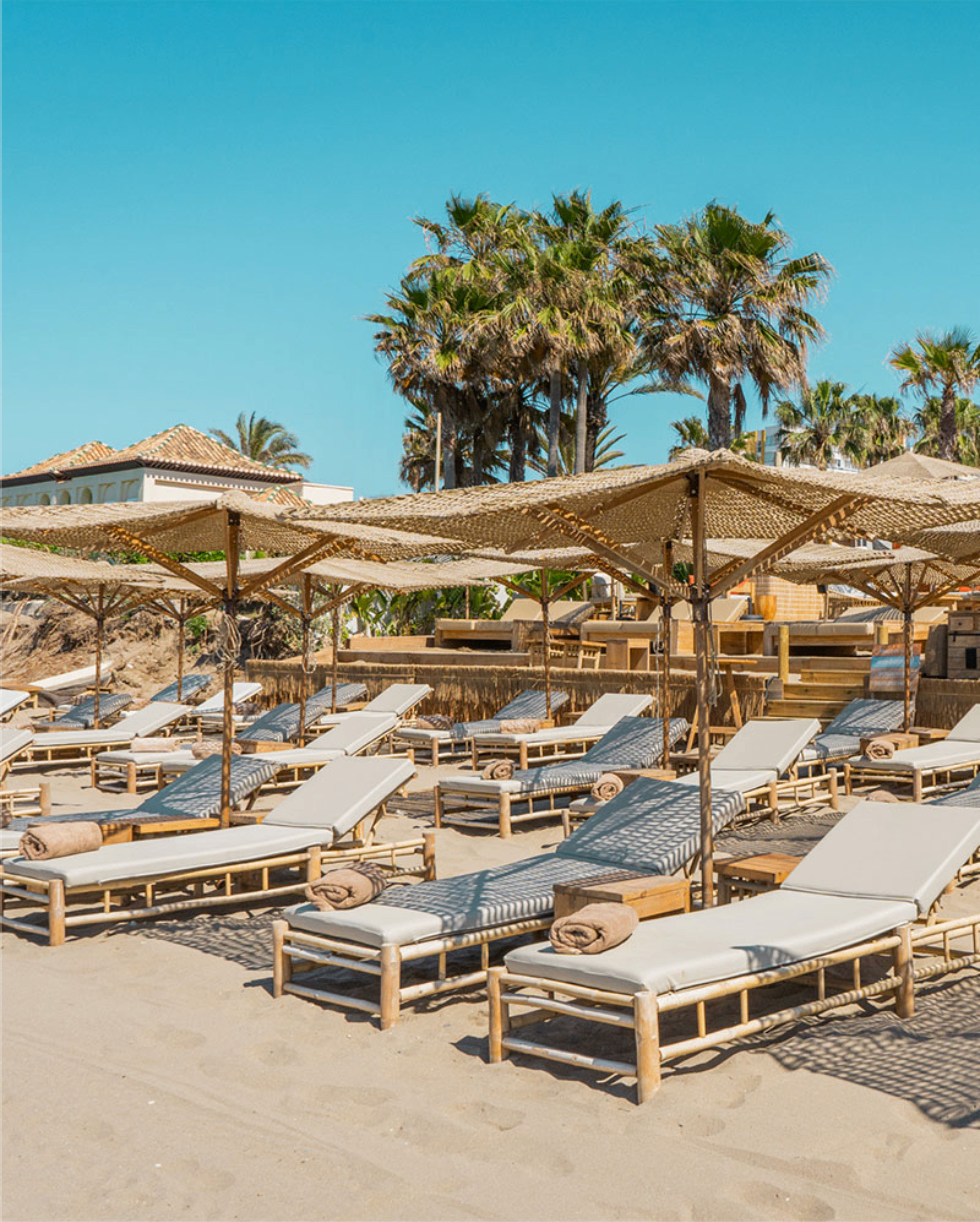 Rows of sunbeds and woven parasols at Nosso Summer Club Marbella on the sand