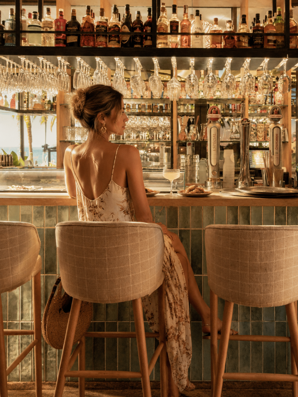 Guest seated at the bar inside Alabardero Beach Club beneath hanging glasses and warm light